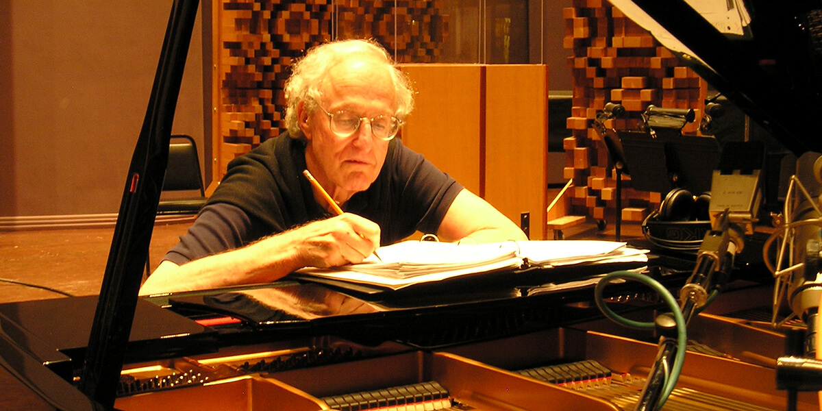 Photo of David Shire writing in a binder while sitting at a piano